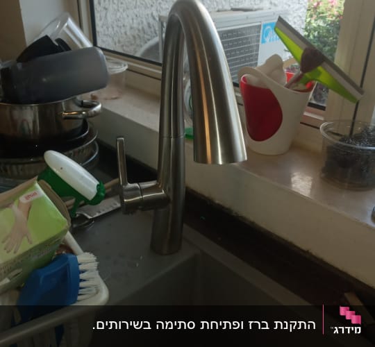ברז נירוסטה בכיור מטבח עם כלים מסביב